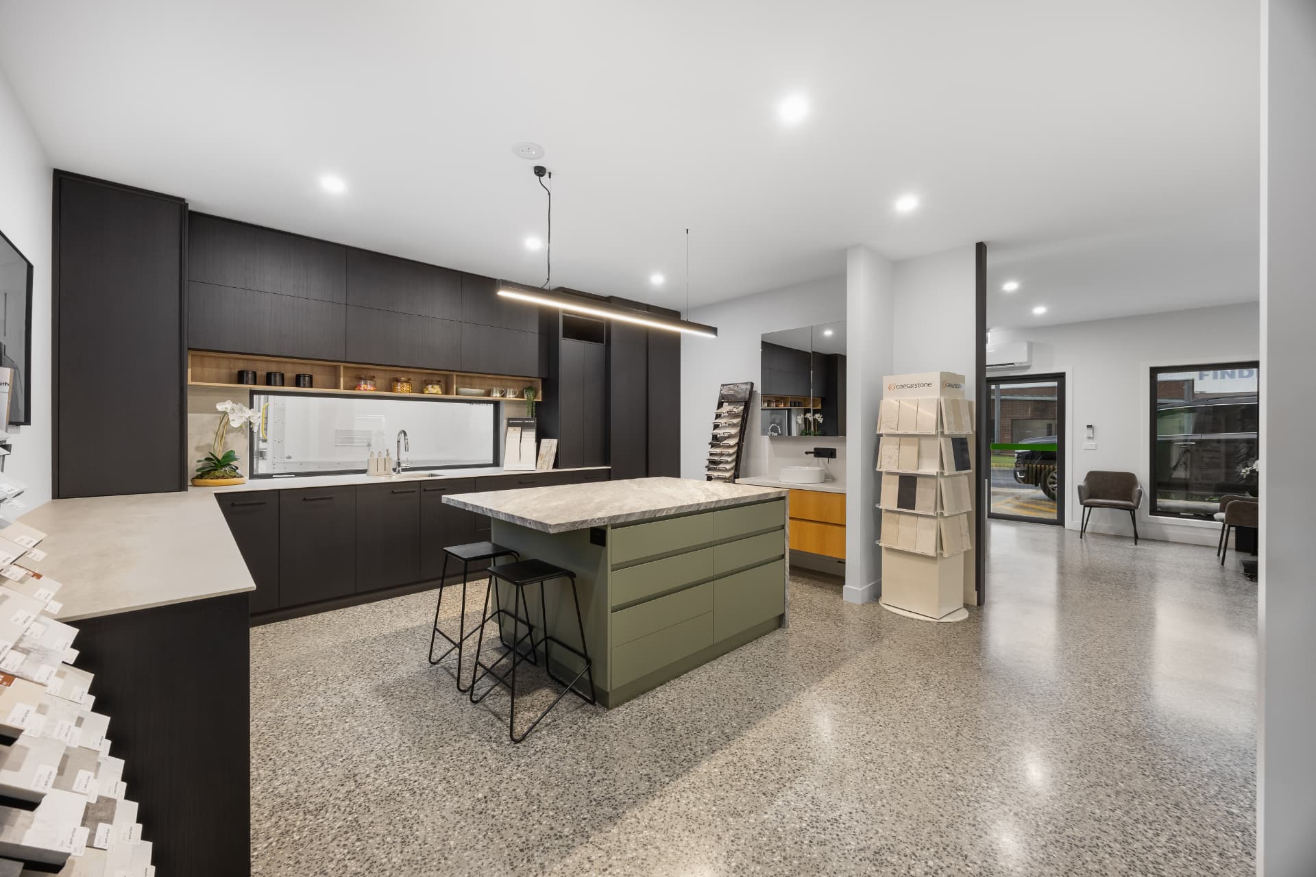 Display kitchen with dark cabinetry, olive green island and stone benchtop