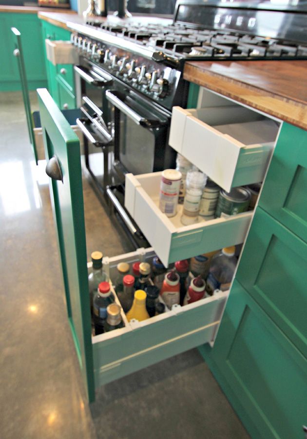 Blum deep kitchen drawers storing bottles and condiments in a green kitchen
